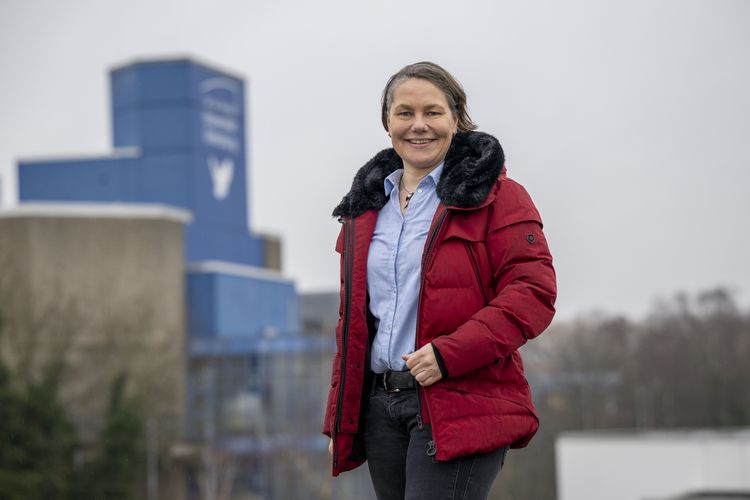 Das Bild zeigt Saskia Gertzen. Sie steht auf dem Dach eines Gebäudes der Universität und lächelt in die Kamera. Im Hintergrund ist der blaue Turm mit dem Logo der Uni und der Friedenstaube zu erkennen.